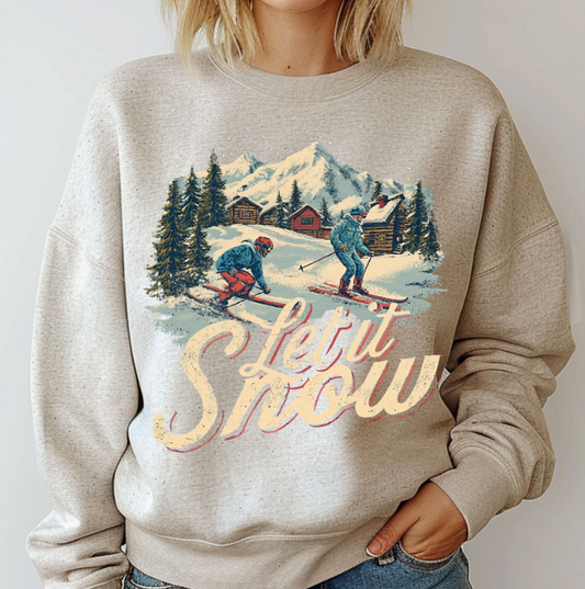 Beige sweatshirt with a winter scene and 'Let it Snow' text worn by a person.